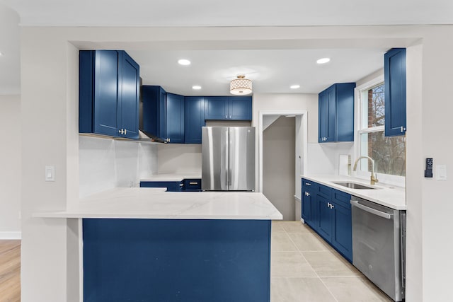 kitchen with appliances with stainless steel finishes, blue cabinets, a sink, and a peninsula