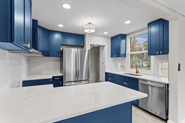 kitchen featuring appliances with stainless steel finishes, a sink, light stone counters, and blue cabinetry