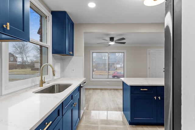 kitchen with baseboards, a sink, light stone countertops, blue cabinetry, and stainless steel dishwasher