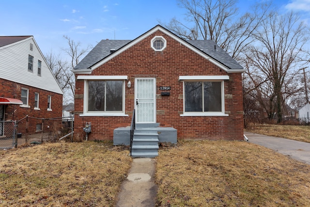 bungalow with a shingled roof, fence, and brick siding