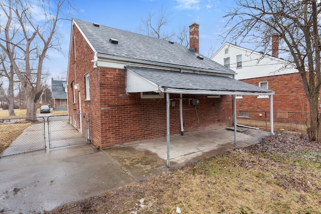 rear view of house with a gate, brick siding, fence, and roof with shingles