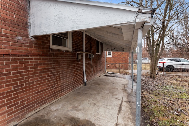 view of side of home featuring fence, a carport, and brick siding