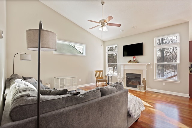 living area featuring lofted ceiling, ceiling fan, wood finished floors, a fireplace with flush hearth, and baseboards