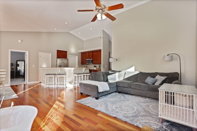 living room featuring baseboards, a ceiling fan, light wood-style flooring, high vaulted ceiling, and recessed lighting