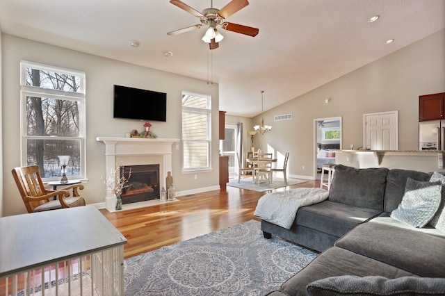 living room featuring ceiling fan with notable chandelier, wood finished floors, visible vents, and baseboards