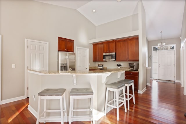 kitchen with baseboards, a kitchen bar, appliances with stainless steel finishes, and dark wood-type flooring