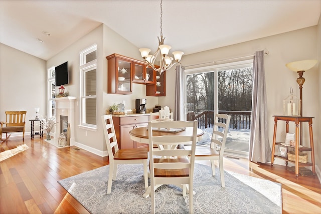 dining room with light wood-style floors, a glass covered fireplace, vaulted ceiling, and an inviting chandelier