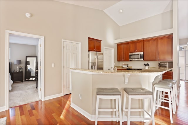 kitchen featuring light wood finished floors, baseboards, appliances with stainless steel finishes, a breakfast bar area, and high vaulted ceiling