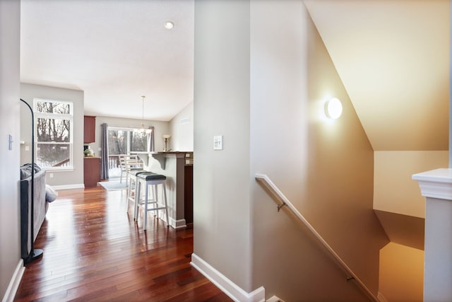 hallway with dark wood-type flooring, baseboards, an upstairs landing, and an inviting chandelier