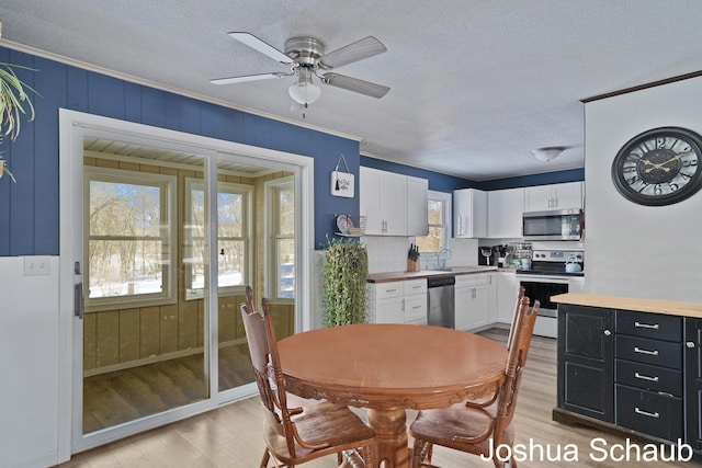 dining area featuring a textured ceiling, ceiling fan, ornamental molding, and light wood-style floors