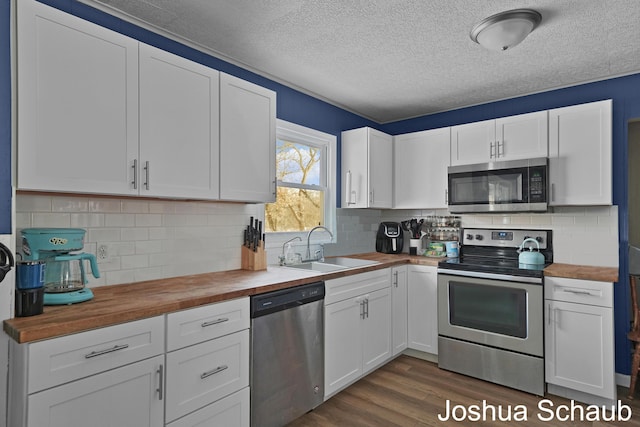 kitchen with dark wood-style floors, wooden counters, appliances with stainless steel finishes, white cabinetry, and a sink