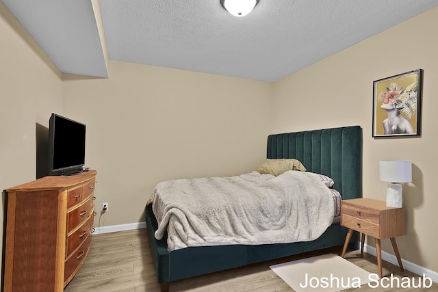 bedroom featuring a textured ceiling, baseboards, and wood finished floors