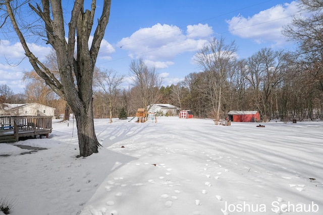 yard layered in snow featuring a shed, a deck, and an outbuilding