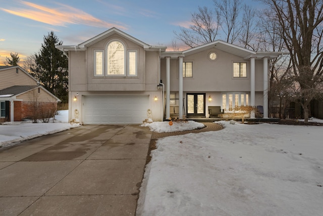 view of front facade with driveway, an attached garage, covered porch, french doors, and stucco siding