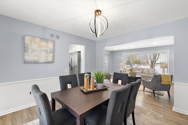 dining area with a notable chandelier, light wood-type flooring, visible vents, and baseboards