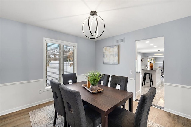 dining area with light wood finished floors, an inviting chandelier, visible vents, and baseboards