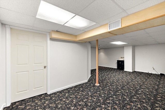 finished below grade area featuring carpet floors, visible vents, a drop ceiling, and baseboards