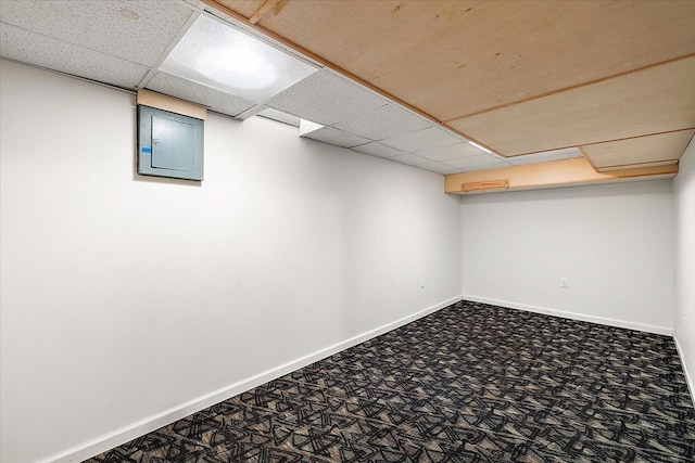 finished below grade area with carpet, electric panel, a paneled ceiling, and baseboards