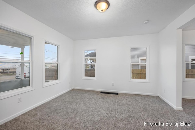 carpeted empty room featuring visible vents, a textured ceiling, and baseboards