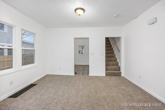 empty room featuring baseboards, visible vents, stairs, a textured ceiling, and carpet flooring