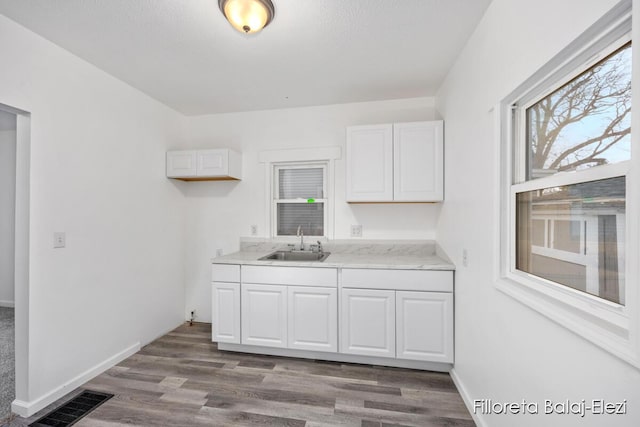 kitchen with dark wood-type flooring, visible vents, white cabinets, and a sink