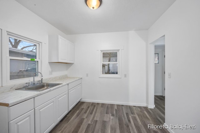 kitchen with baseboards, dark wood-type flooring, light countertops, white cabinetry, and a sink