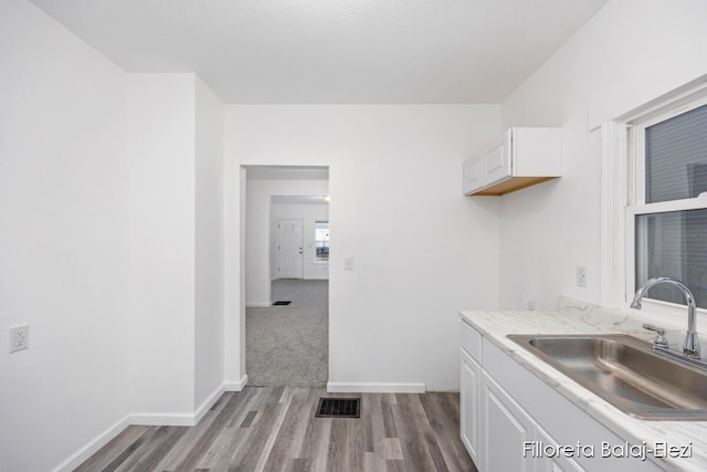 kitchen with wood finished floors, a sink, visible vents, white cabinetry, and light countertops