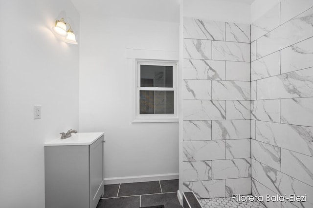 bathroom with a tile shower, vanity, baseboards, and tile patterned floors