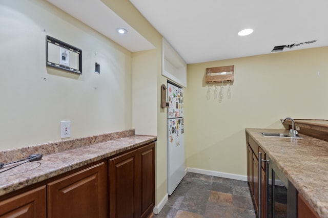 kitchen featuring beverage cooler, baseboards, stone finish flooring, light countertops, and a sink