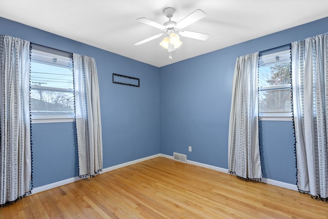 unfurnished room with plenty of natural light, wood finished floors, visible vents, and baseboards