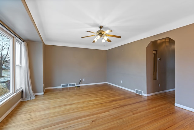 empty room featuring light wood-style floors, baseboards, visible vents, and arched walkways