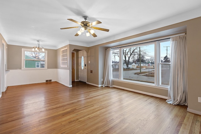 interior space with arched walkways, visible vents, light wood-style flooring, baseboards, and ceiling fan with notable chandelier