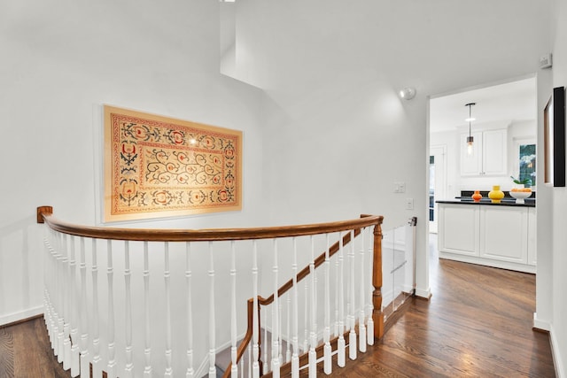 hall with dark wood-style flooring, baseboards, and an upstairs landing