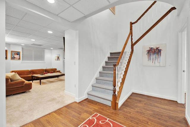 interior space featuring baseboards, arched walkways, wood finished floors, stairs, and a paneled ceiling