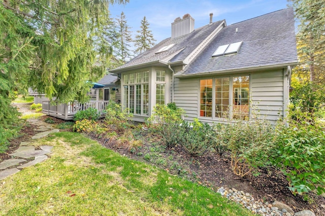 rear view of property featuring a shingled roof, a chimney, a deck, and a lawn