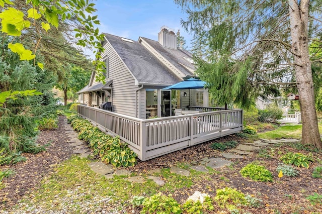 back of property featuring a chimney, a deck, and roof with shingles