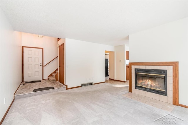 unfurnished living room with light carpet, a fireplace, visible vents, baseboards, and stairs