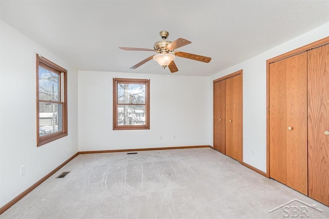 unfurnished bedroom with two closets, visible vents, a ceiling fan, light carpet, and baseboards