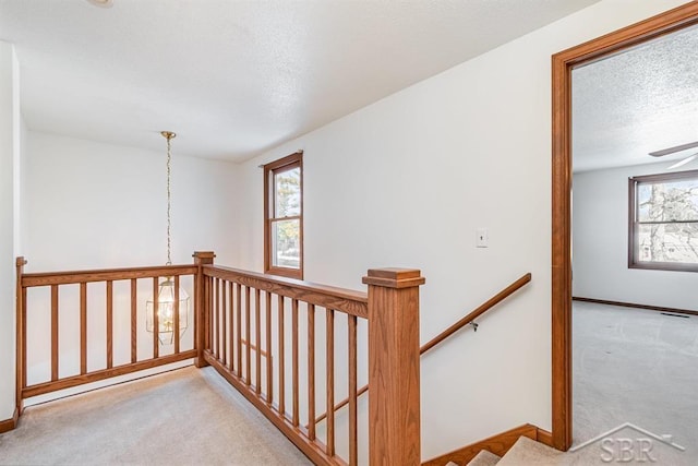 corridor featuring a textured ceiling, carpet floors, an upstairs landing, and baseboards