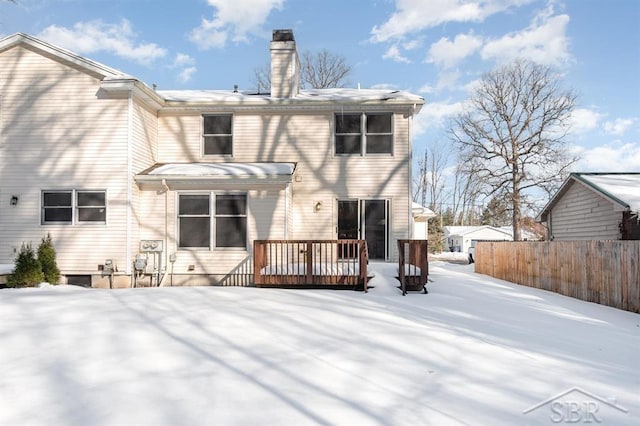 snow covered house featuring a chimney, fence, and a wooden deck