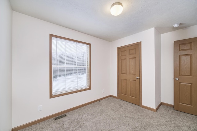 unfurnished bedroom featuring baseboards, visible vents, a textured ceiling, and light colored carpet