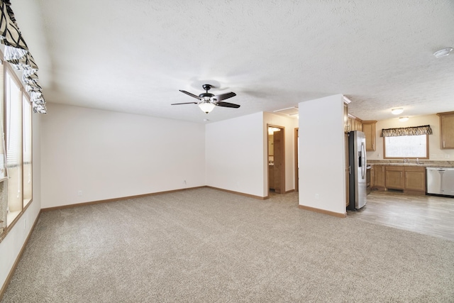 unfurnished living room featuring ceiling fan, baseboards, a textured ceiling, and light colored carpet