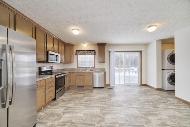 kitchen featuring stacked washer / dryer, a sink, baseboards, appliances with stainless steel finishes, and brown cabinets