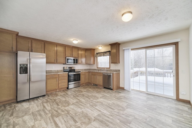 kitchen with light countertops, appliances with stainless steel finishes, brown cabinetry, a sink, and a textured ceiling