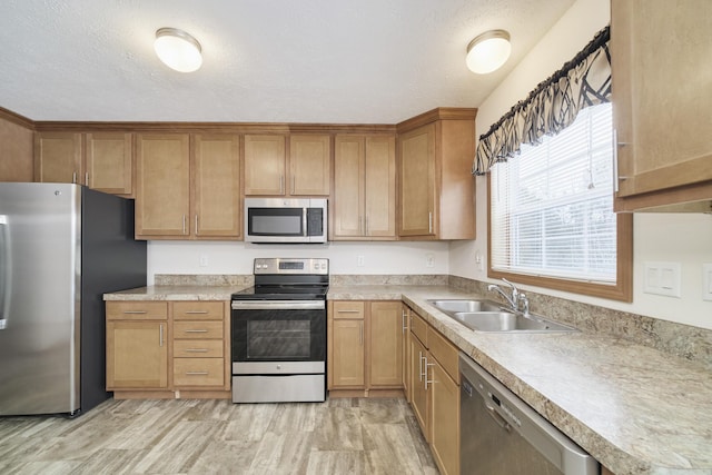 kitchen with a textured ceiling, light countertops, appliances with stainless steel finishes, and a sink