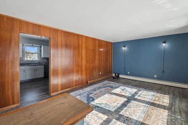 spare room featuring dark wood-style flooring, baseboard heating, a sink, and wooden walls