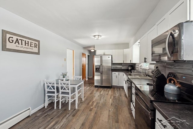 kitchen featuring a baseboard radiator, a sink, appliances with stainless steel finishes, backsplash, and dark countertops