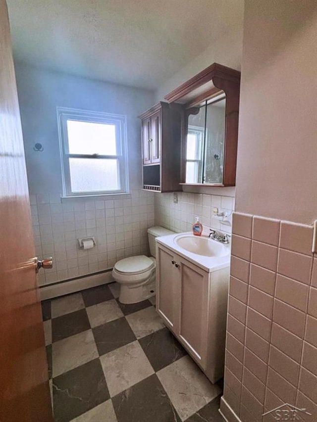 half bathroom featuring toilet, a baseboard heating unit, vanity, tile walls, and tile patterned floors