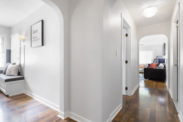 corridor featuring arched walkways, baseboards, and hardwood / wood-style flooring