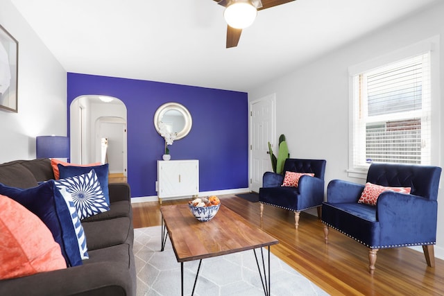 living area with arched walkways, wood finished floors, a ceiling fan, and baseboards